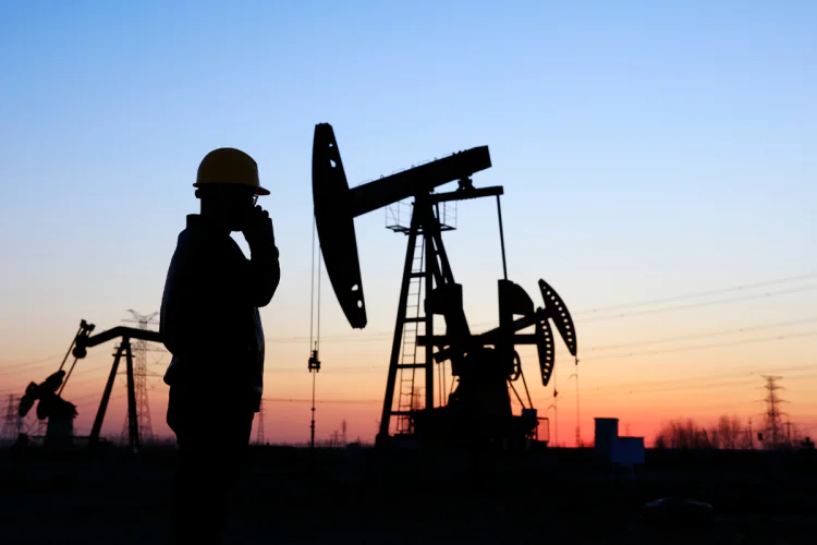 Worker and oil derrick silhouetted at sunset