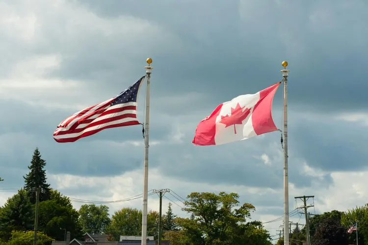 Canadian and United States flags blowing in the wind.