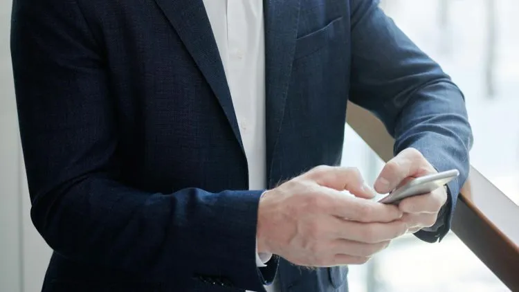 Man in a blue suit texting on a phone