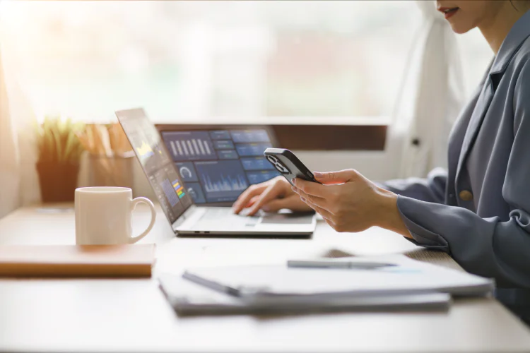 Businessperson holds phone and works on laptop computer