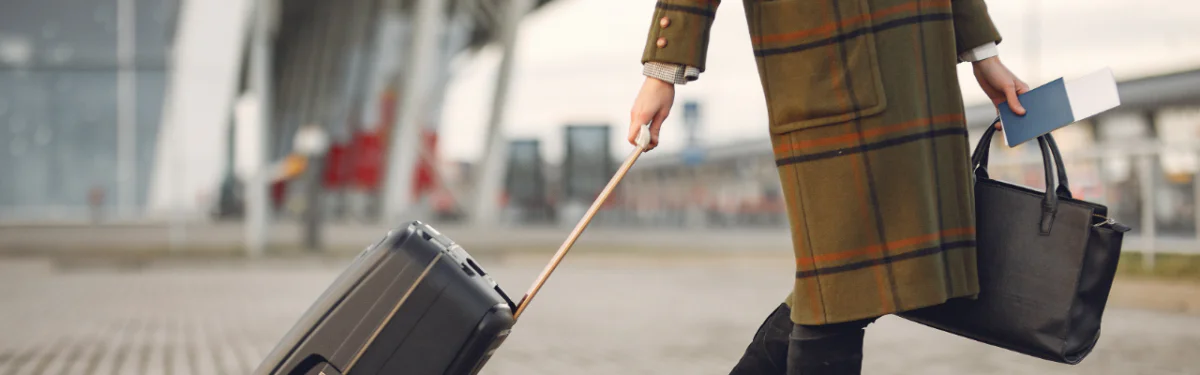 Business woman with plaid wool coat carries passport and purse and pulls rolling suitcase