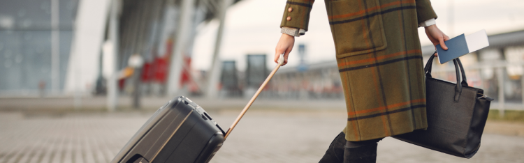 Business woman with plaid wool coat carries passport and purse and pulls rolling suitcase