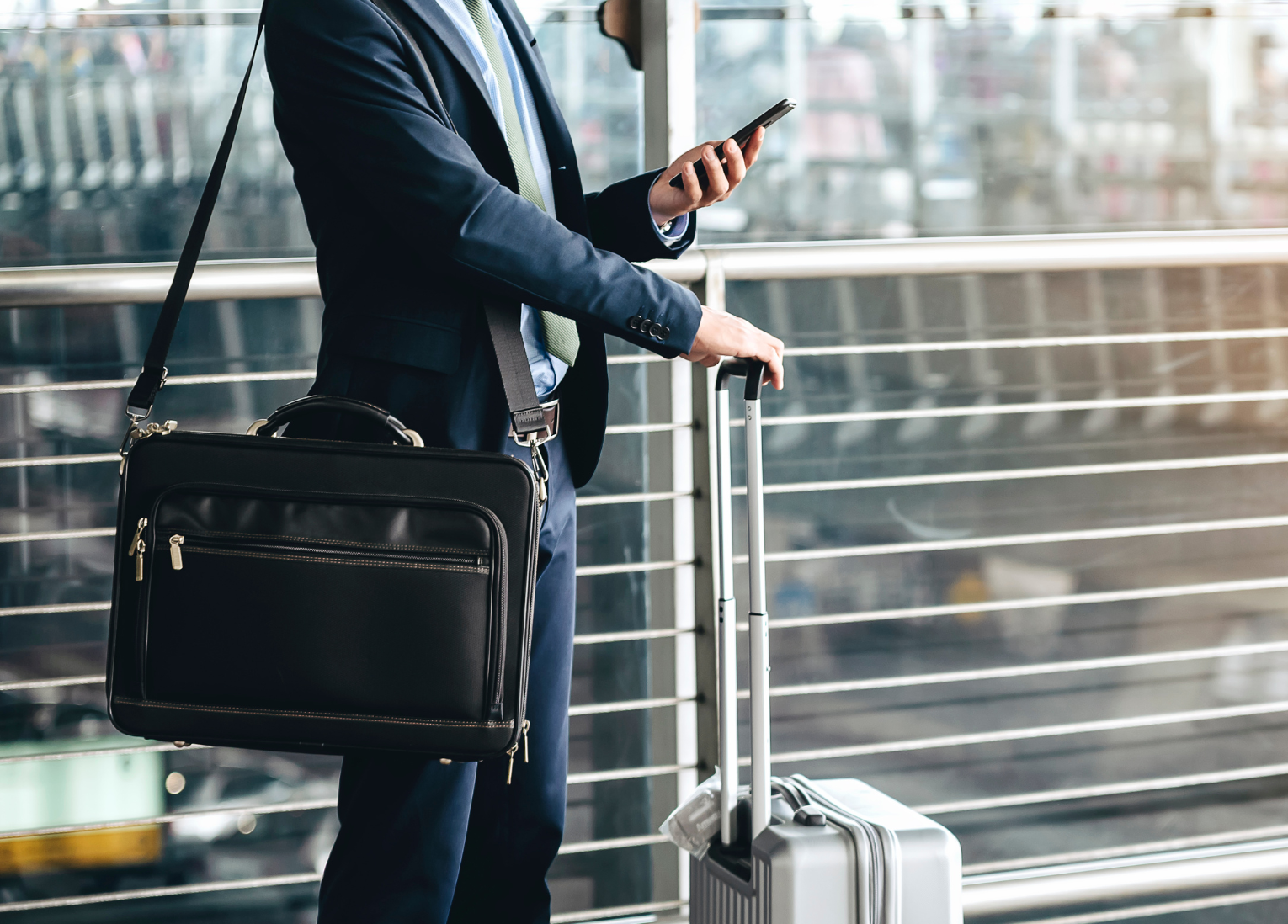 Business person with briefcase and rolling luggage holds cellphone