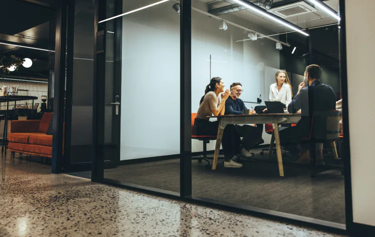 Business team sits around table in modern office space with glass wall