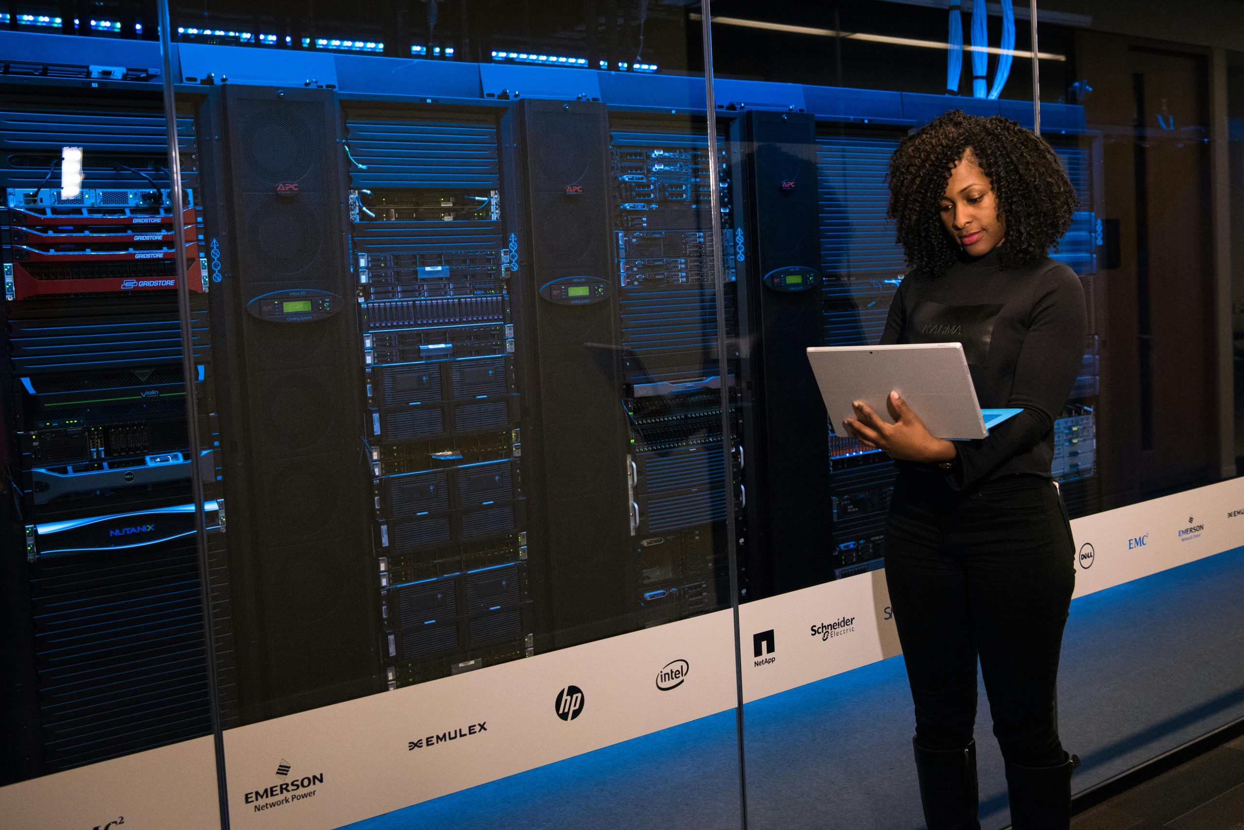 Female IT worker stands with open laptop outside of a server room