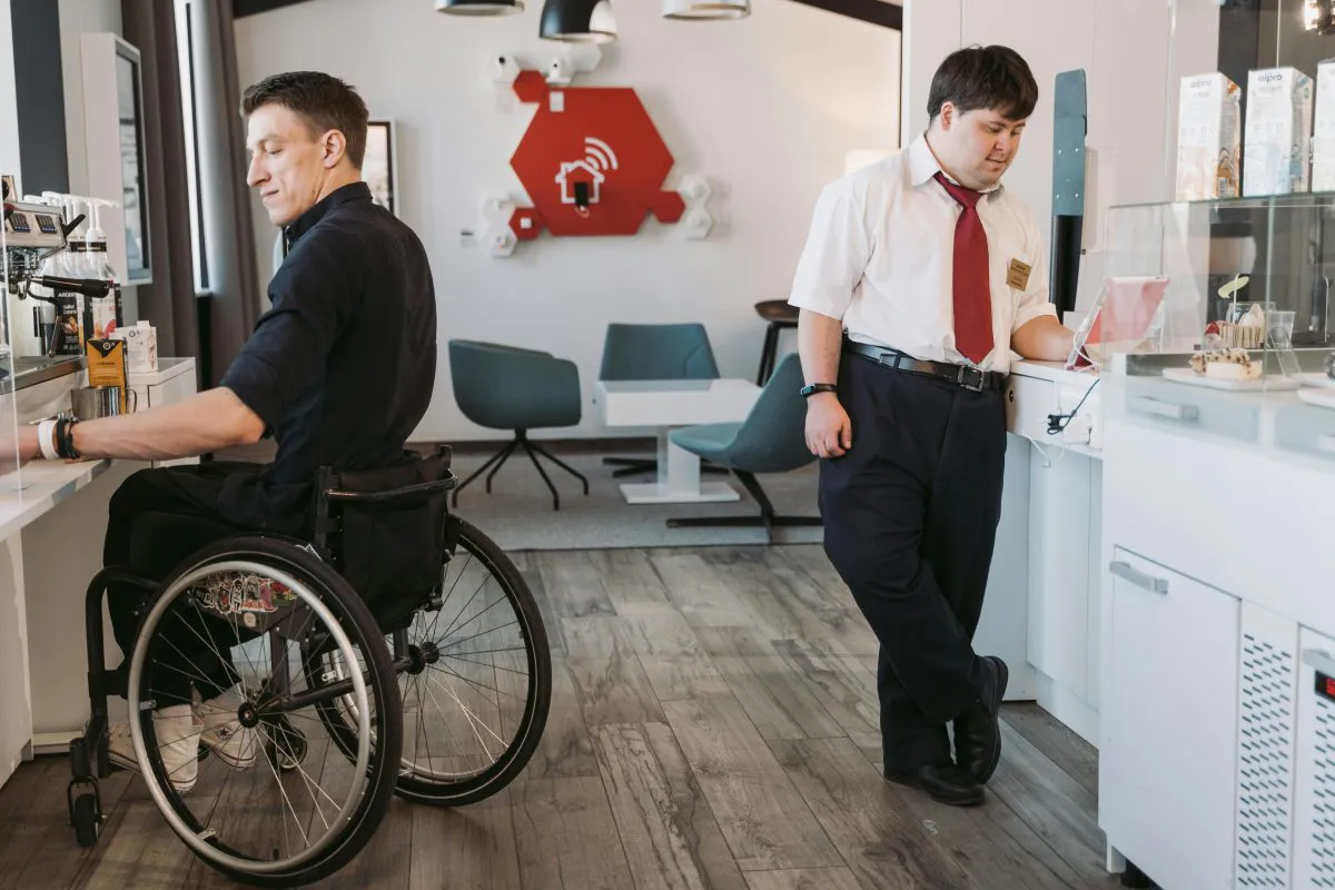 Man in wheelchair makes coffee and main in white shirt uses iPad in a cafe