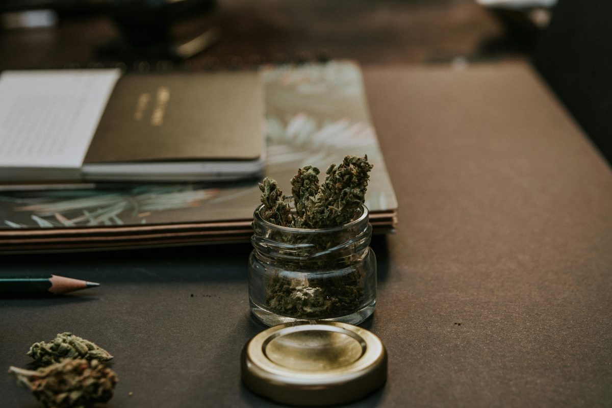 Cannabis product in glass jar next to notebooks and pencil