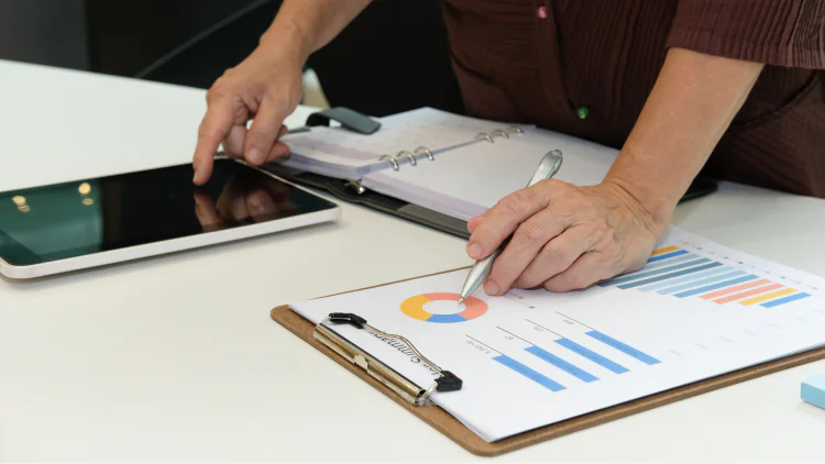 A close-up of someone's hands as they cross-reference information between a tables and clipboard