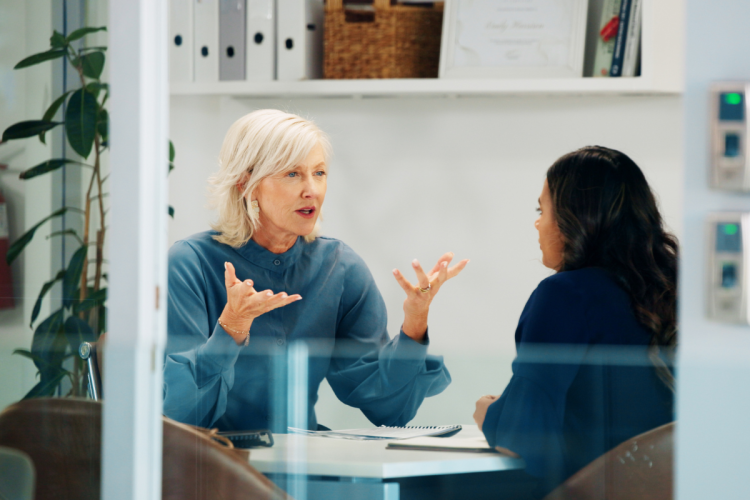 Two women sit at office table in serious conversation