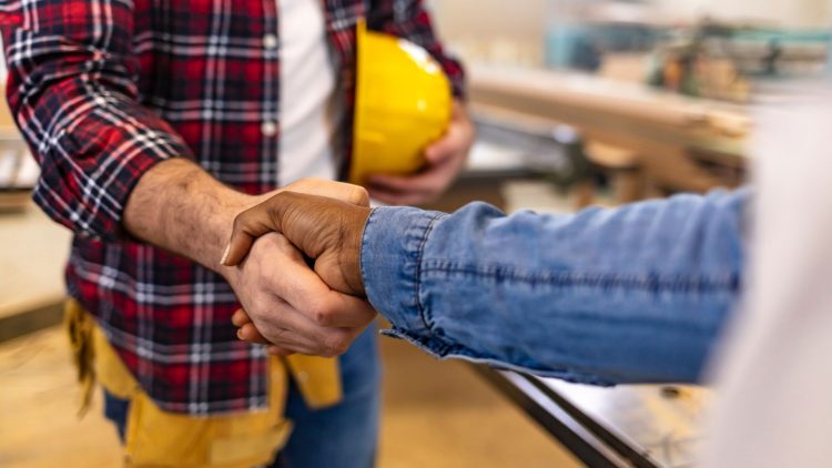 A person in flannel holding a hard hat shakes another person's hand at a job site