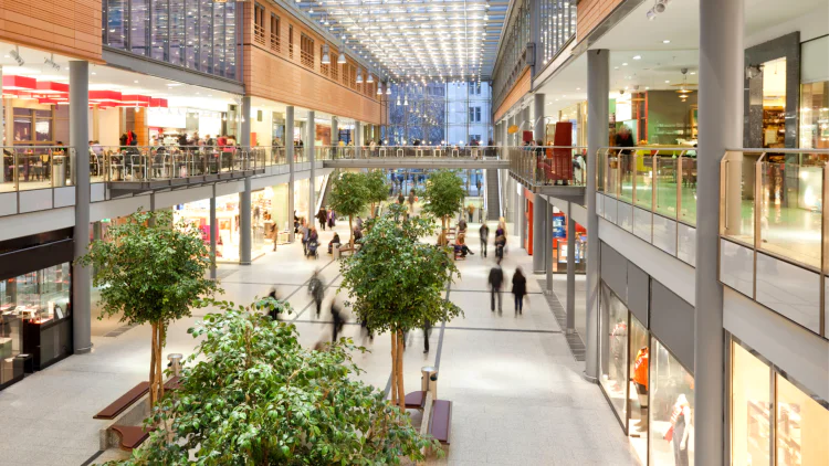 A photo of the inside of a mall. The centre aisle is lined with trees.