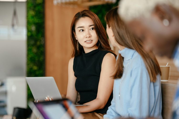 Two business women in conversation, serious expressions, one holds laptop