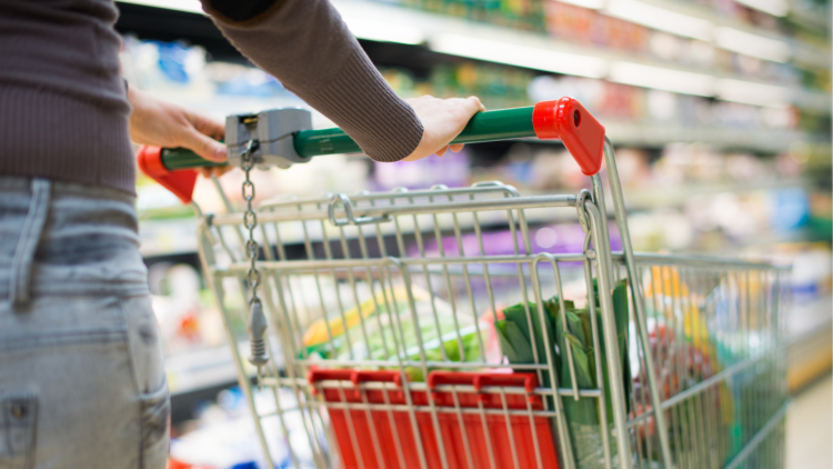 A close up of someone pushing a shopping cart down a supermarket aisle.