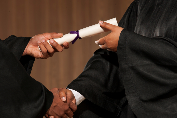 A closeup of a person receiving a diploma at a graduating ceremony