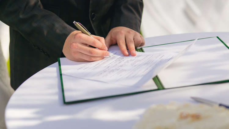 A close-up photo of someone in a suit signing a contract