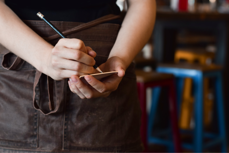 A close up photo of a server writing down an order on their notepad in a restaurant