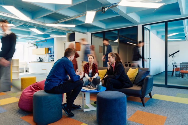 Multiethnic startup business team on meeting in a modern bright open space coworking office. Brainstorming, working on laptop. Group of coworkers walking around in motion blur.