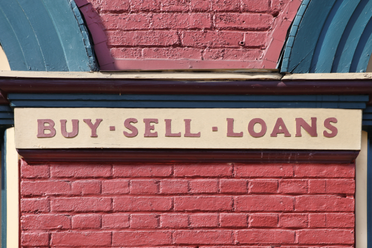 A close up image of a pawn shop sign that read Buy, Sell, Loan against a red brick background
