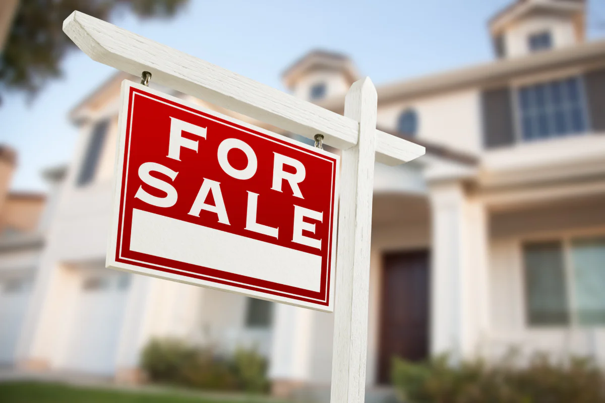 A photo of a for sale sign in front of a large, modern-looking home