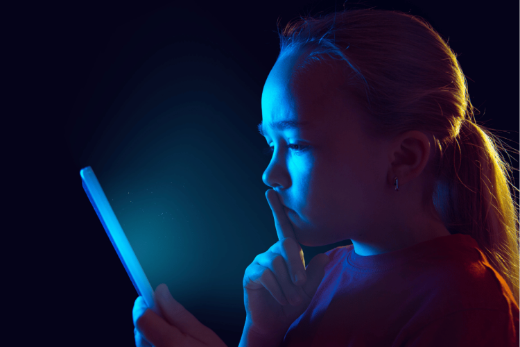 A concerned-looking youth looking at a tablet screen in a dark room