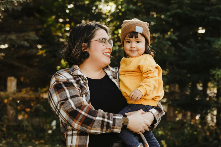 An Indigenous mother holding her child, smiling, outdoors during the day