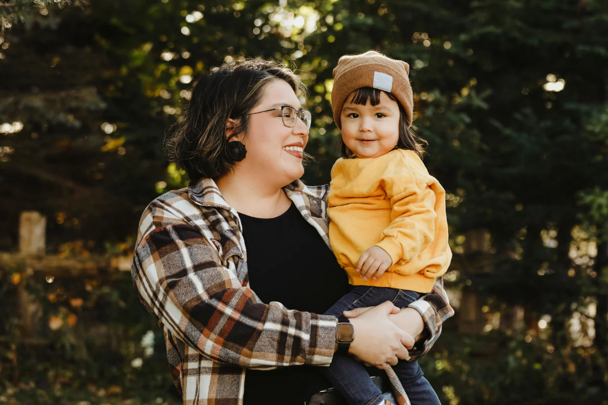 An Indigenous mother holding her child, smiling, outdoors during the day