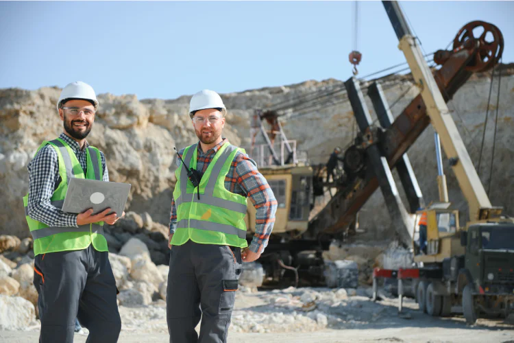 Two men in safety gear standing in front of mining equipment