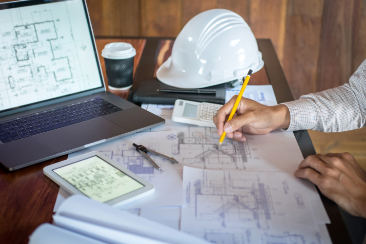 An out-of-frame person working on blueprints in a jobsite office