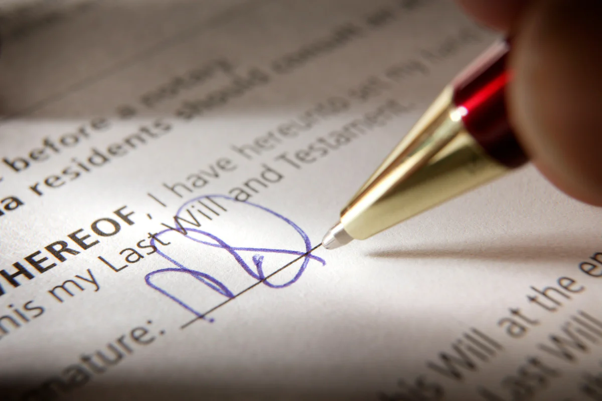 A closeup photo of a person holding a pen as they sign their will