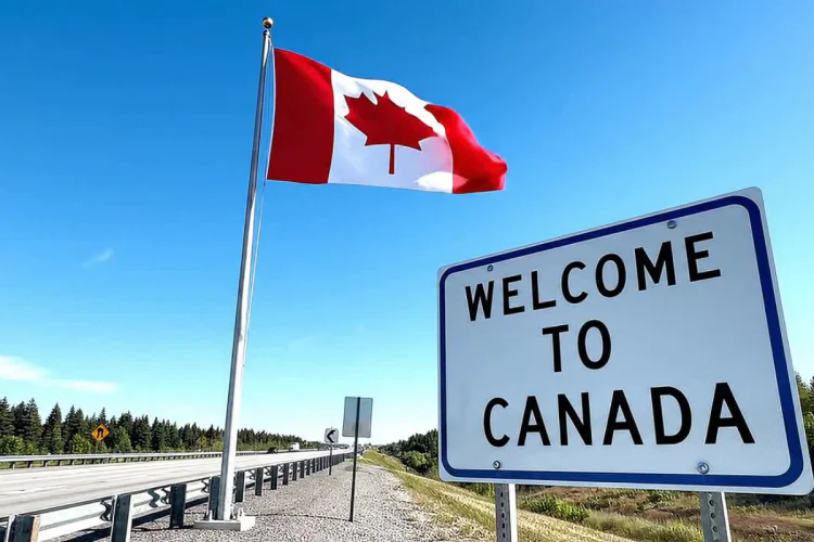 A "Welcome to Canada" sign with a Canadian flag waving in the background by a highway