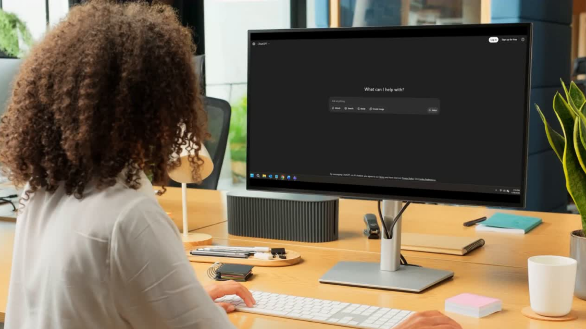 Business woman sits at office desk, looking at ChatGPT on monitor
