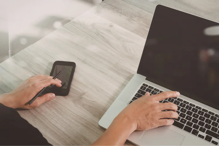 A closeup of someone working on a laptop and a cell phone