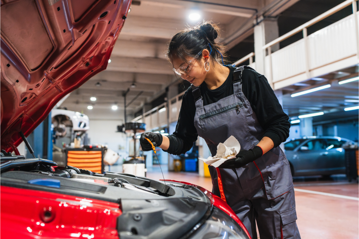 An autobody repair tech checking the oil in a car while in a repair shop.