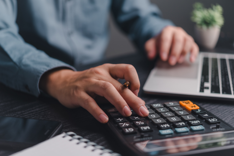 A man doing payroll work on a calculator and laptop
