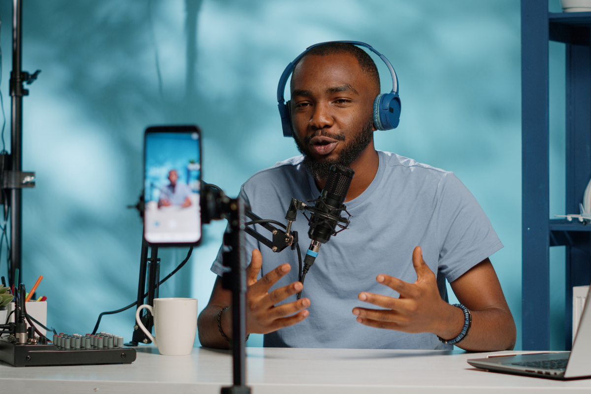 A content creator speaking into a mic in a home studio while being filmed on a cell phone