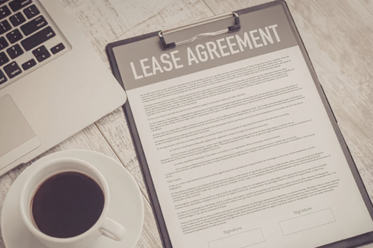 A lease agreement on a clipboard near a laptop and cup of coffee on a desk