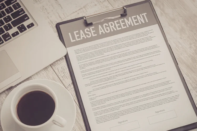 A lease agreement on a clipboard near a laptop and cup of coffee on a desk