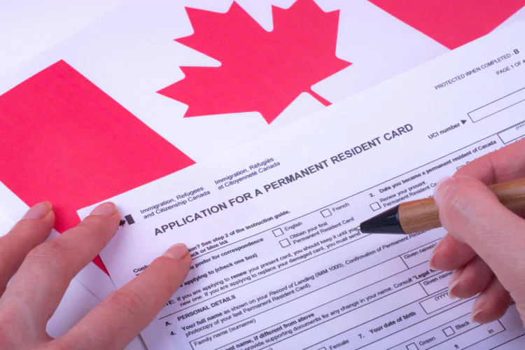 A person filling out a permanent residency form over a Canadian flag