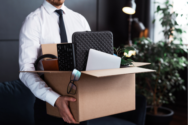 A recently-fired employee carrying his personal items out of an office in a cardboard box