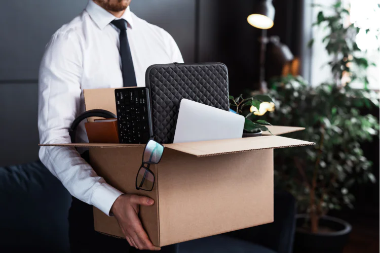A recently-fired employee carrying his personal items out of an office in a cardboard box