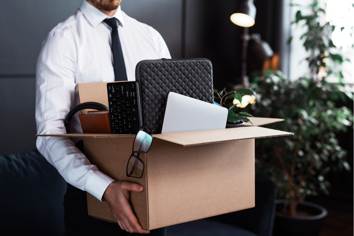 A recently-fired employee carrying his personal items out of an office in a cardboard box