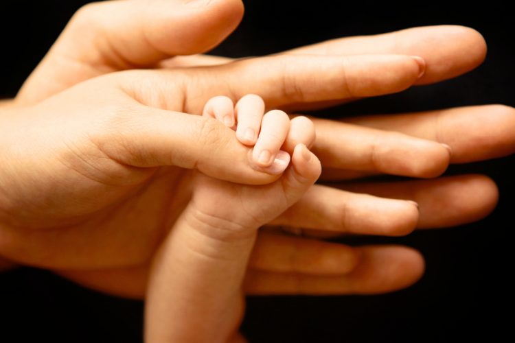 A baby hand holding onto an adult's thumb