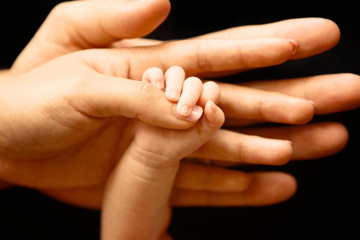 A baby hand holding onto an adult's thumb