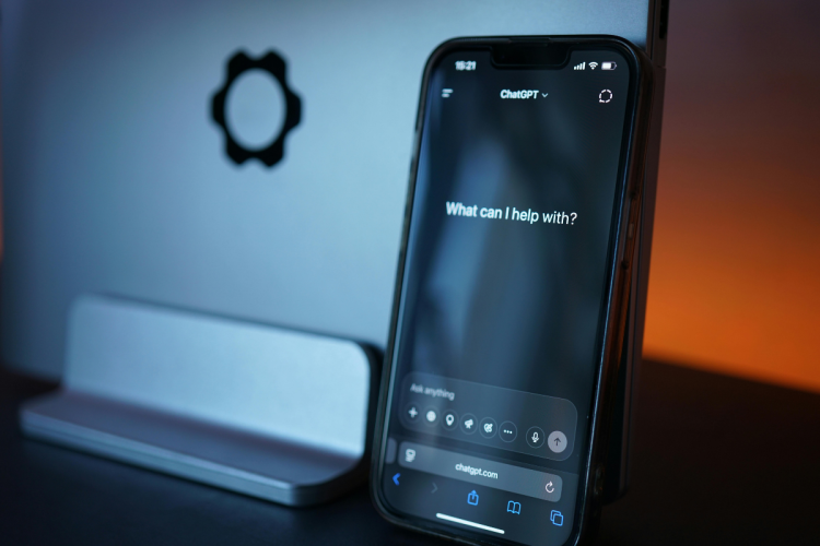 A phone with chatGPT open in a dimly lit room, a laptop in the background