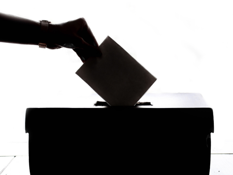 A silhouetted hand placing a ballot in a ballot box