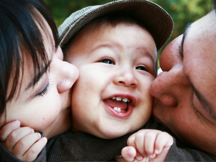 Two parents kissing the cheeks of a smiling child