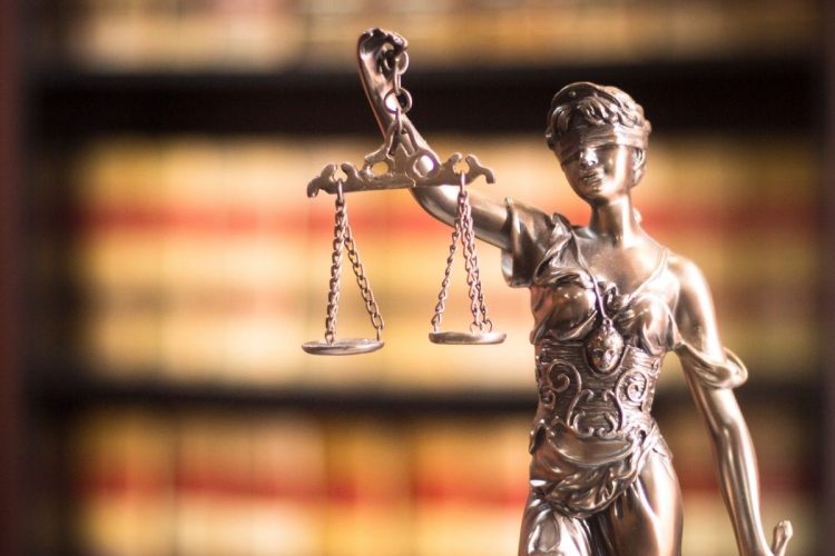 A statue of Lady Justice against a background bookshelf