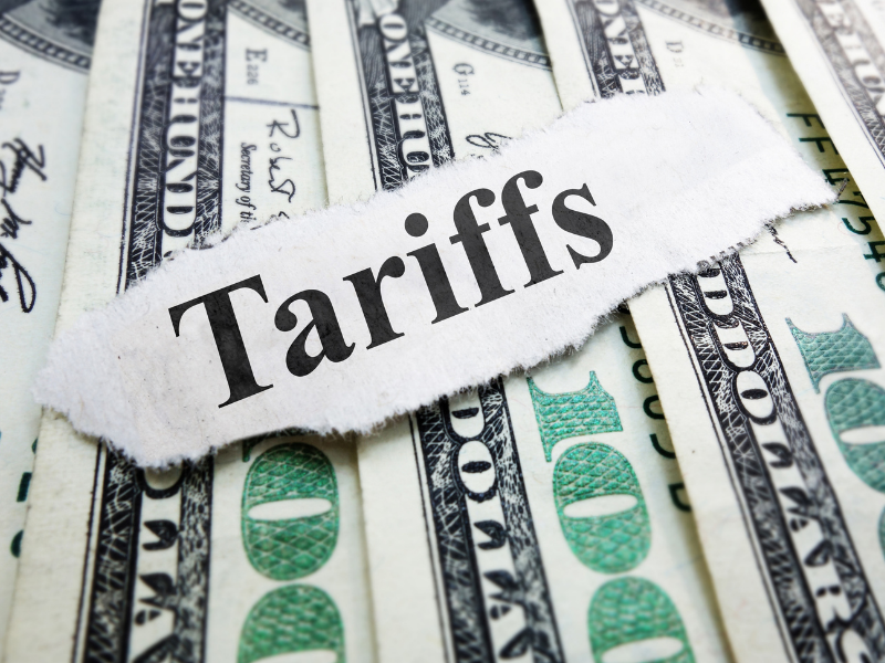Cut out lettering spelling tariffs on top of a pile of U.S. $100 bills