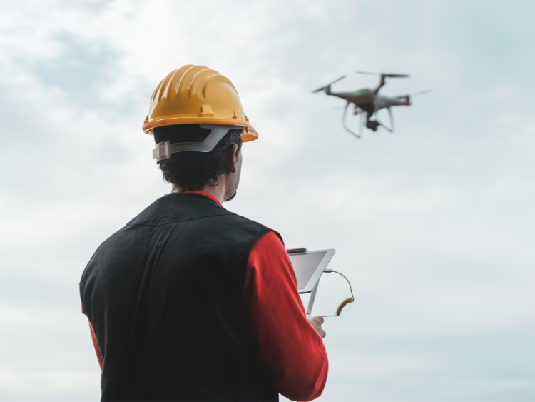 A worker piloting a drone against a cloudy sky