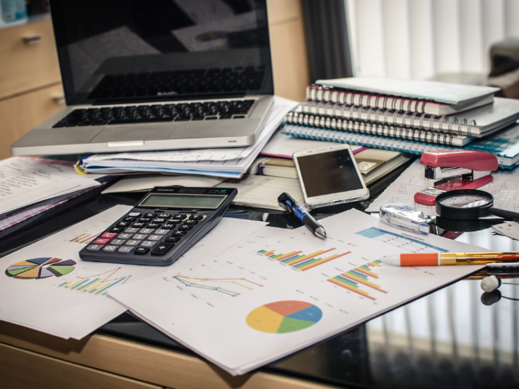 Laptop, calculator and papers scattered across a desk